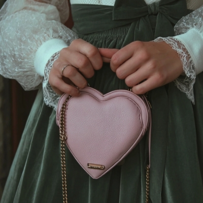 Alle Must-have Make-Up Produkte für die Trachtentasche Model in Dirndl hält eine rosa herzförmige Handtasche