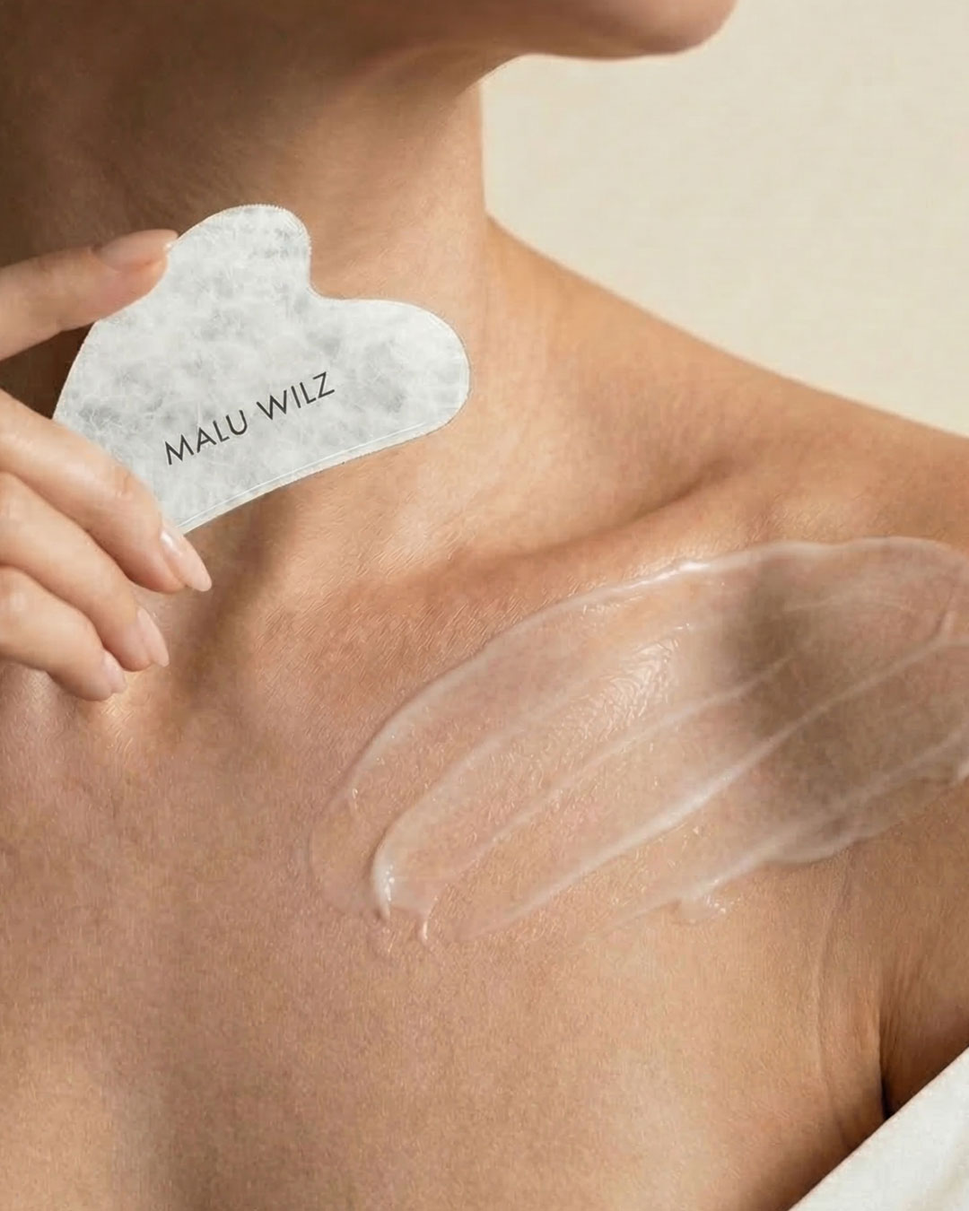 Frau h&auml;lt Gua Sha Stein in der Hand und hat auf dem Dekollet&eacute; Creme