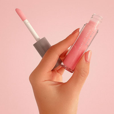 Das Luxury Lip Serum pflegt die Lippen und taucht sie in einen Hauch Farbe. Hand hält rosa Lippenserum