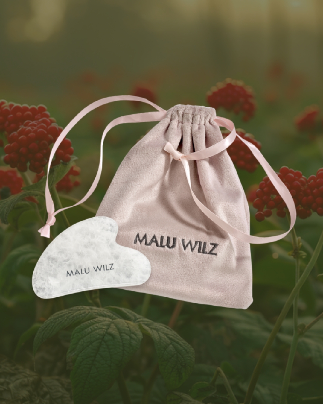 Massagetool für das Power of Ginseng Treatment Rosa Samtbeutel mit Malu Wilz Logo und Gua Sha Stein vor Ginseng-Blüten